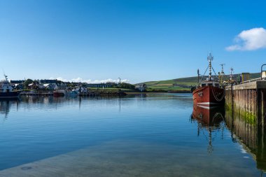 Dingle, Ireland - 7 August, 2022: red fishing boat on the docks of Dingle Harbor in County Kerry with reflections in the calm water