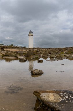 A view of the historic Southerness Lighthouse in Scotland with reflections in tidal pools in the foreground