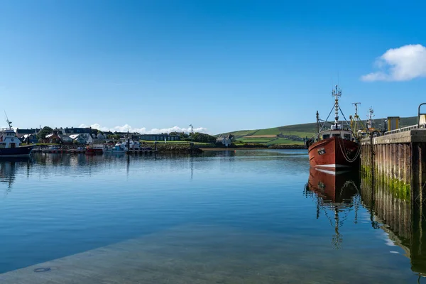 Dingle, Ireland - 7 August, 2022: red fishing boat on the docks of Dingle Harbor in County Kerry with reflections in the calm water