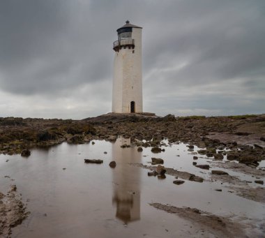 A view of the historic Southerness Lighthouse in Scotland with reflections in tidal pools in the foreground