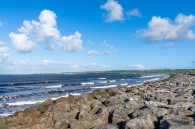 Arka planda Lahinch Sahili 'nde büyük kaya ve dalgaların kırıldığı fırtına erozyon koruma önlemleri