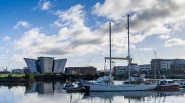 Belfast, Birleşik Krallık - 21 Ağustos 2022: arka planda Titanik müzesi olan Lagan Nehri üzerindeki Belfast 'ın Titanik Mahallesi' nde limana ve marinaya demirlemiş yelkenliler