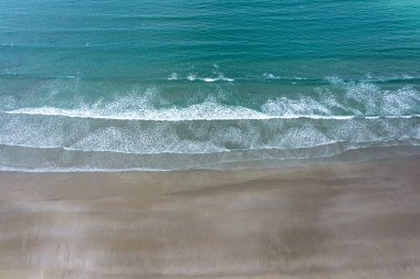Turkuaz okyanus ve beyaz kaplama dalgaların boş bir kumsalda kırılışını gösteren tepeden aşağı insansız hava aracı görüntüsü.