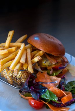 Lezzetli bir çizburger ve patates kızartmasının dikey görüntüsü. Taze sebzelerle dolu bir sepetin içinde.