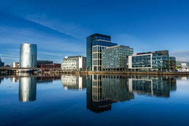 Belfast, Birleşik Krallık - 21 Ağustos 2022: Belfast şehir merkezinin gökdelenleri ve yansımaları ile şafak vakti sakin nehir Lagan 'da