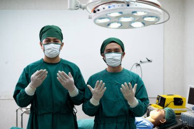 İki doktor ameliyathanede yeşil maskeli cerrahi cerrah saç kepi eldivenli biri yatağın önünde diğeri de elektrik defibrilatörü takıyor..