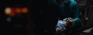 Hasta ameliyat odasındaki cerrahi yatağın üzerine uzanmış bir solunum cihazı takıyor. Yanında cerrah var. Gece vakti hastanede belirtilere dikkat etmek için yanında durun.