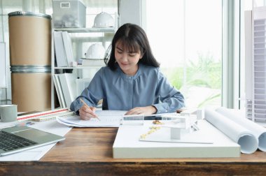 Profesyonel mimar kadınlar tasarım işlerinde çalışırken modern ev modelinin taslağını hazırlıyorlar. Çatı katında malzeme örneği ve dizüstü bilgisayarı var..