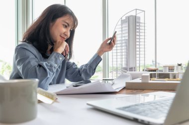 Tasarımcı olarak çalışan profesyonel mimar kadınlar modern ev için malzeme örneklerini masanın üzerinde tutuyorlar ve çatı katındaki ofisin planına, materyal örneğine ve bina modeline sahipler.