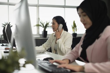 Diz üstü bilgisayar ve klavyenin önünde kendine güvenen kadın çalışanlarıyla dolu bir müşteri hizmetleri ofisi.