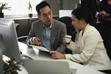 Yönetim çalışanları ofis çalışanlarına günlük not defterinde iş projesini anlatıyor ve bir ofis çalışma alanını işaret ediyor..