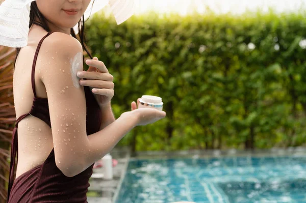 Young Asian women white skin applying suntan lotion while sunbathing by the swimming pool, prevent sunburn and skincare concept