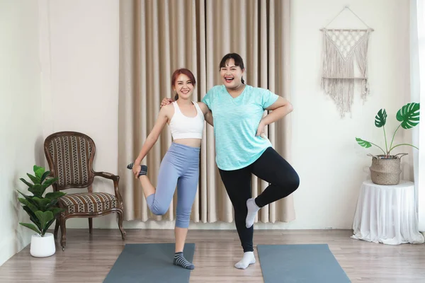 Fat woman practicing yoga with yoga instructor and looked at camera inviting them to practice yoga. Flexible body and manage body to be strong. How to practice yoga for obese women or overweight