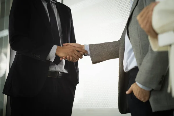 Businessman in smart office suit shaking their hands with partners after successfully negotiated business together at front of meeting room unclear mirror wall.