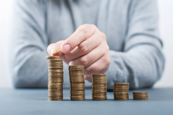 A man's hand puts a coin into a pile. The concept of accumulating or saving money. Close-up 