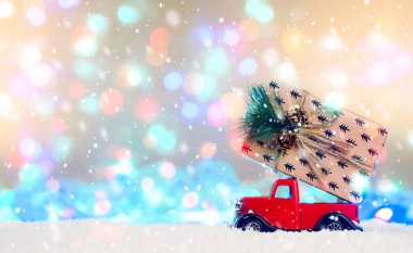 Kırmızı bir araba, karda parlak mavi ışıkların arka planına karşı bir hediye taşır. Teslimat. Noel ve Yeni Yıl konsepti. Boşluğu kopyala 