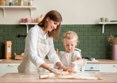 Genç bir anne ve küçük kızı mutfakta birlikte yemek pişiriyorlar. Anne ve çocuk evde hamur pişirecek.