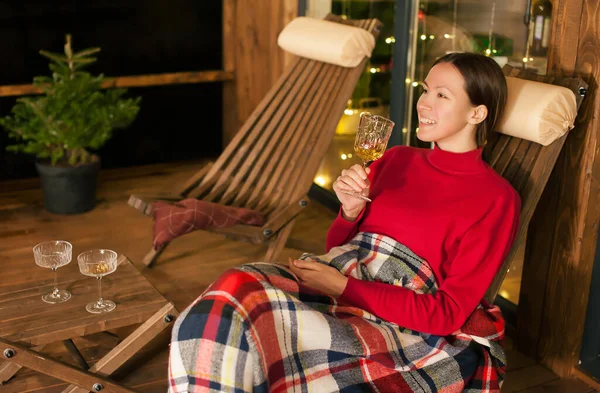 Akşamları evin terasında elinde bir bardak şarapla mutlu bir kız Noel 'i kutluyor. odağını kaldır