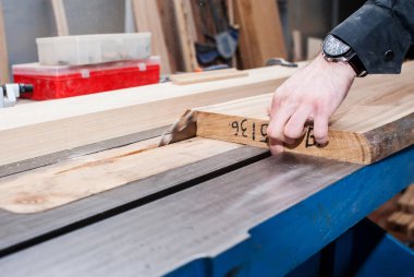 Erkek marangoz, bir marangoz atölyesinde sabit dairesel testere tahtasını kesiyor.