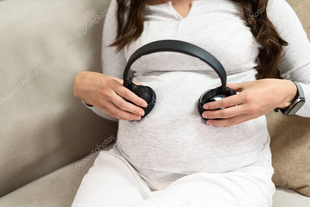 closeup pregnant mom with headphones on tummy sitting on couch, chatting with baby