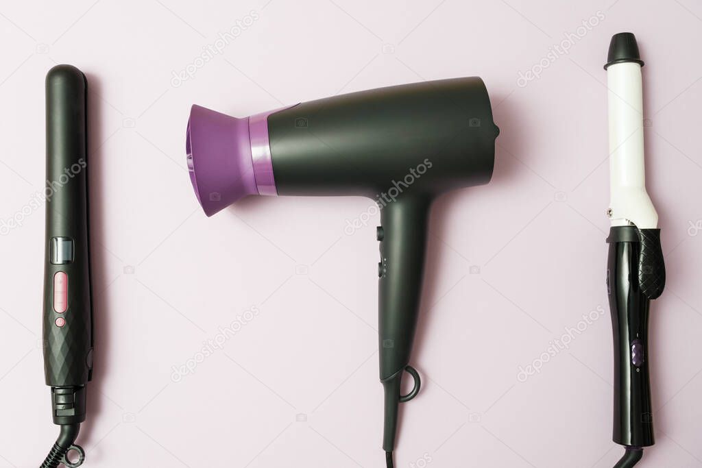 professional hairdresser set, top view hair dryer, curling iron, straightener in black on purple background