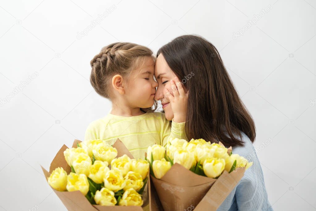mother and baby hug, unconditional love, mother's day concept, little girl and woman with closed eyes and bouquet of yellow tulips
