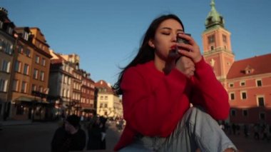 Genç güzel Asyalı kız sokakta sigara içiyor, kırmızı kazak ve kırmızı gül, modern, Varşova Polonya