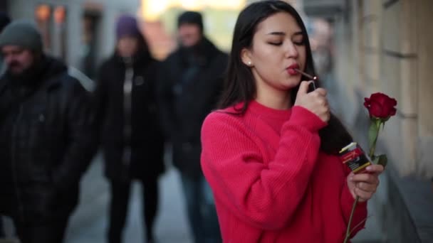 若い美しいアジアの女の子は通りにタバコを吸う 赤いセーターと赤いバラ 近代的な ワルシャワのポーランド — ストック動画