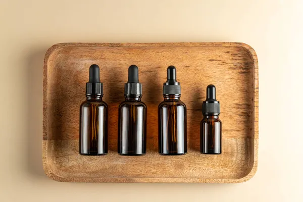 Dark glass cosmetic bottles of different size with face serum or essentioal oil on a wooden background. Unbradned Beauty cosmetic products