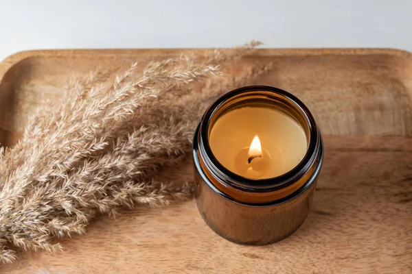 Handmade candle from paraffin and soy wax in glass jar with dry reed grass on wooden tray. Candle making