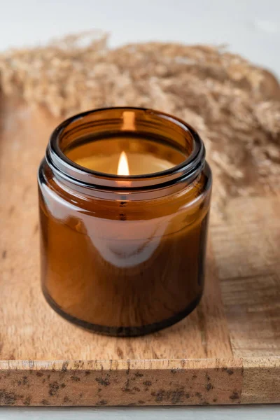 Burning aroma candle in a glass jar with the aroma of spices. Autumn atmosphere with dry reeds grass. Cosy lifestyle.