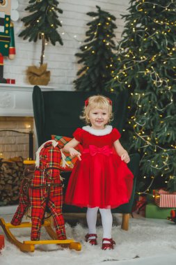 Baby girl at Christmas eve. girl on toy horse gurney in festive Christmas interior before New Year. Entertainment for holidays.