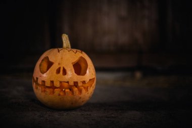 Halloween pumpkin head jack in dark barn on wooden floor. Scary background for poster of celebration of Halloween. Copy space