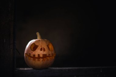 Halloween pumpkin head jack in dark barn on wooden floor. Scary background for poster of celebration of Halloween. Copy space