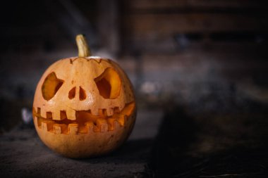 Halloween pumpkin head jack in dark barn on wooden floor. Scary background for poster of celebration of Halloween. Copy space