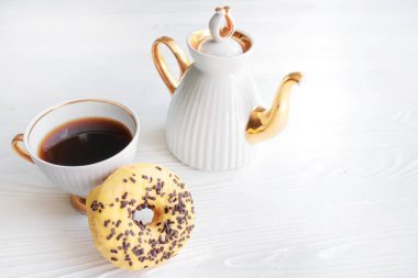 white porcelain teapot and cup on white background on sunny day. Banana doughnut with chocolate chips for a sweet breakfast