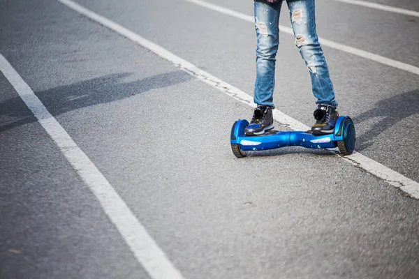 legs of girl in ripped jeans riding on blue gyroboard ontracks in stadium in city. Active lifestyle. Useful gadgets for sports. Person on white hoverboard. Electriic hyroscooter driving. Self-balancing two-wheeled board or hoverboard scooter. electri