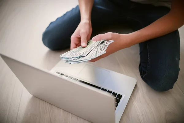 Hands with bundle of money. Teenager counts banknotes while sitting by laptop. Cash bills pouring into freelancer. Easy money earned on online exchanges or remote earnings. Return of savings.