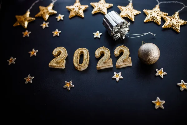 Happy New Year 2022. Holiday background with golden Christmas decorations . 2022 numbers with gold jewelry balls and garland in form of stars.