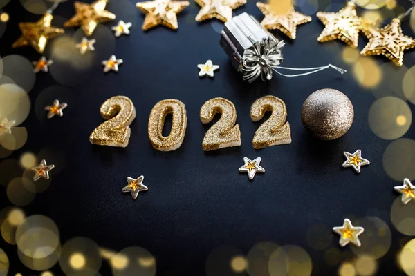 Happy New Year 2022. Holiday background with golden Christmas decorations . 2022 numbers with gold jewelry balls and garland in form of stars.