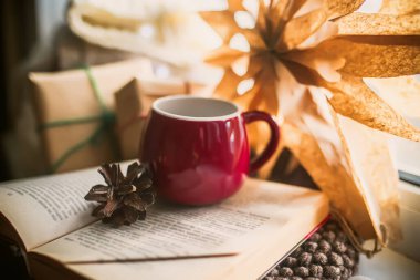 Red cup on the book near the window. Zero waste Christmas concept. DIY home decorations for Christmas. Paper decorations for the new year. Home comfort concept. Selective focus.