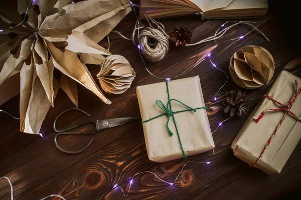 Hand Wrapped Craft Christmas Gift with New Year Lights. Christmas star cut out of craft bags on a wooden table in the evening of the New Year. Selective focus.