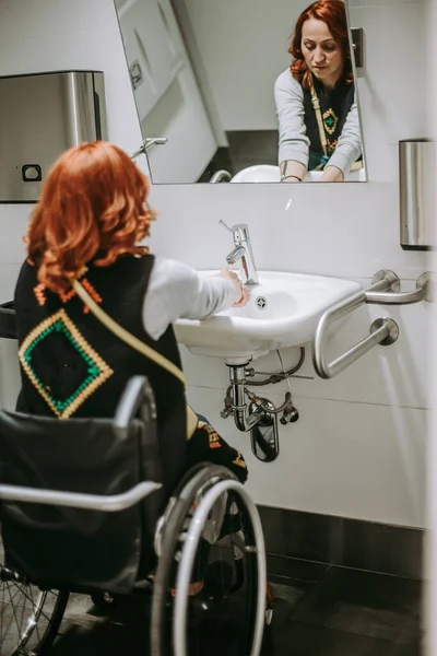 A woman with special needs in a wheelchair washes her hands in a public toilet. Toilet for people with special needs accessible to people in wheelchairs. toilets for disabled