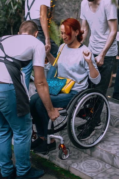 Men help a woman in a wheelchair to descend the stairs not equipped with a ramp for the descent of people with disabilities