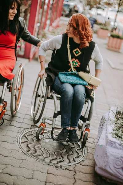 Two girls with special needs in wheelchairs drive through the city streets. Friends on a walk while traveling in Kiev in Ukraine. Selective focus.