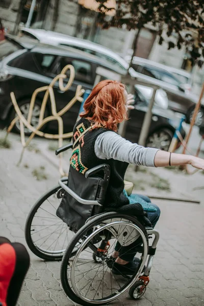 girl in wheelchair rides with hands to side through old town on sidewalk near cars. Freedom of movement of persons with special needs.