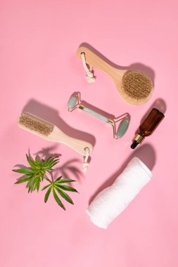 Spa concept with cannabis oil and hemp leaf extract, natural organic spa cosmetics, eco friendly bathroom accessories. Wooden facial cleansing brush with natural bristles and jade beauty roller.