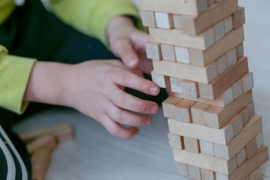 The child plays in a tower of wooden bars. Floors of wooden pieces. The child takes out the bars from the floors of the tower. Board game.