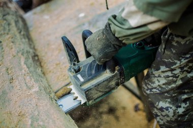 Kalın ağaç gövdesi kabuğu kesen iş elbiseli adam. Erkek ahşap testere sapları.