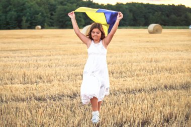 Mavi gökyüzünde dalgalanan Ukrayna bayrağı. Ukrayna bayrağı taşıyan kız gün batımında tarlada koşuyor. Savaşta devlet desteği. Birleşik Avrupa Rusya 'ya karşı. Dünya için umut.